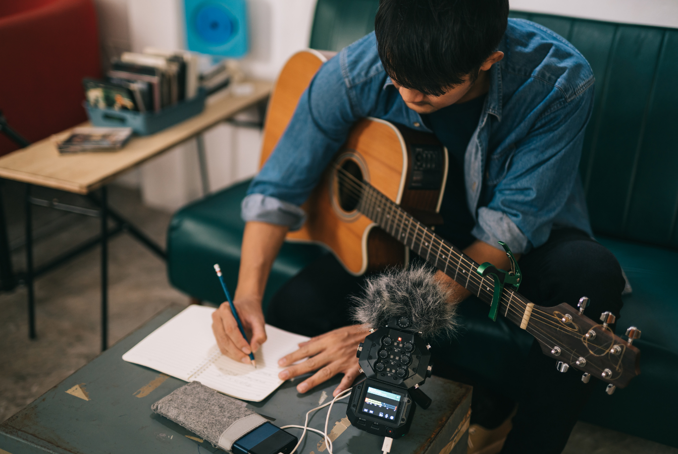 protection-chanson-sacem-creation-musicale.webp Musicien assis avec une guitare acoustique en train d’écrire une chanson dans un carnet, sur une table où se trouve un micro d’enregistrement.